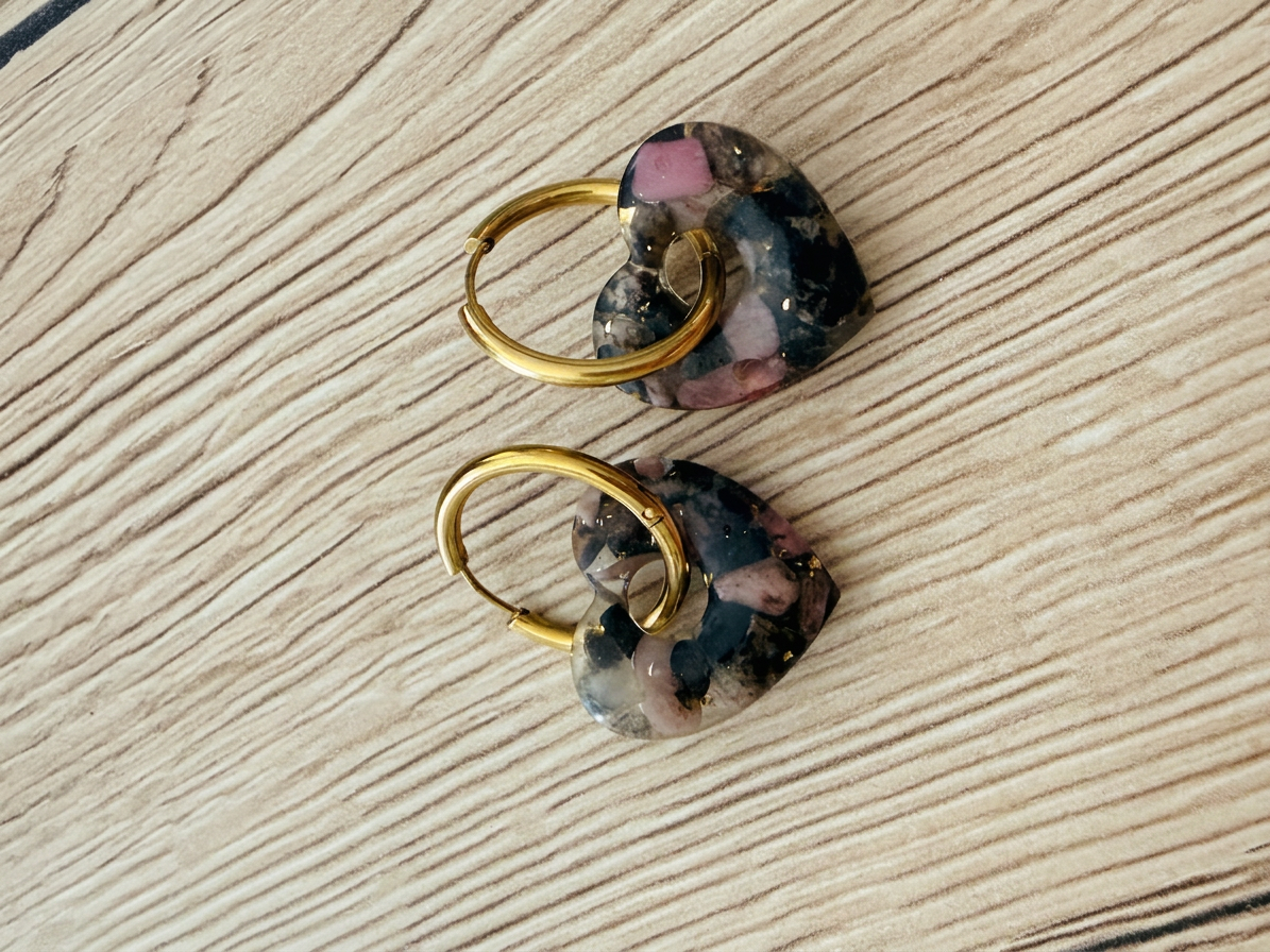 Pair of gold hoop earrings with heart-shaped charms in black, pink, and gray tones
